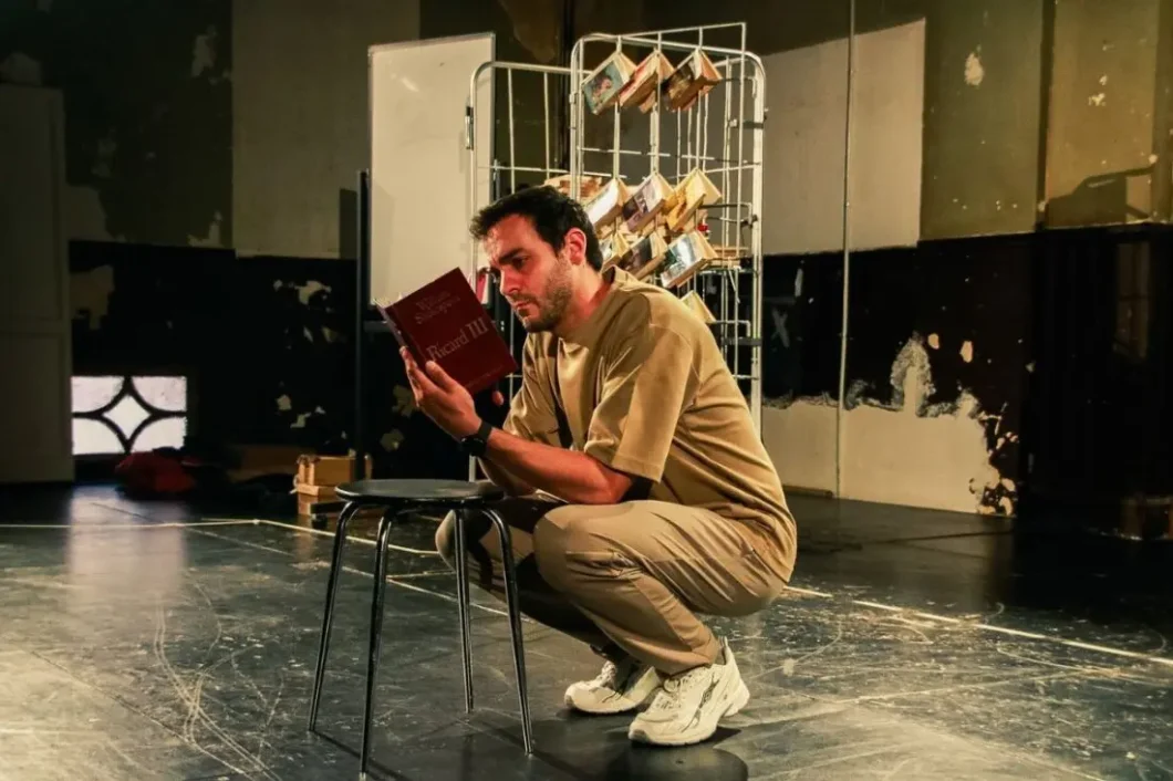 L'actor Quim Àvila en escena, assegut al terra, llegint un exemplar de 'Ricard III' de Shakespeare.