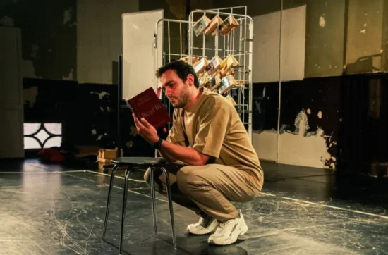 L'actor Quim Àvila en escena, assegut al terra, llegint un exemplar de 'Ricard III' de Shakespeare.